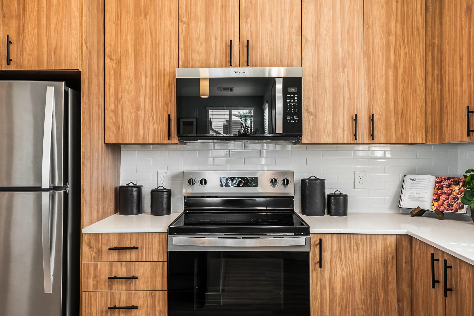 Sonita apartments Modern kitchen with wood cabinets, stainless steel appliances, and white tile backsplash.